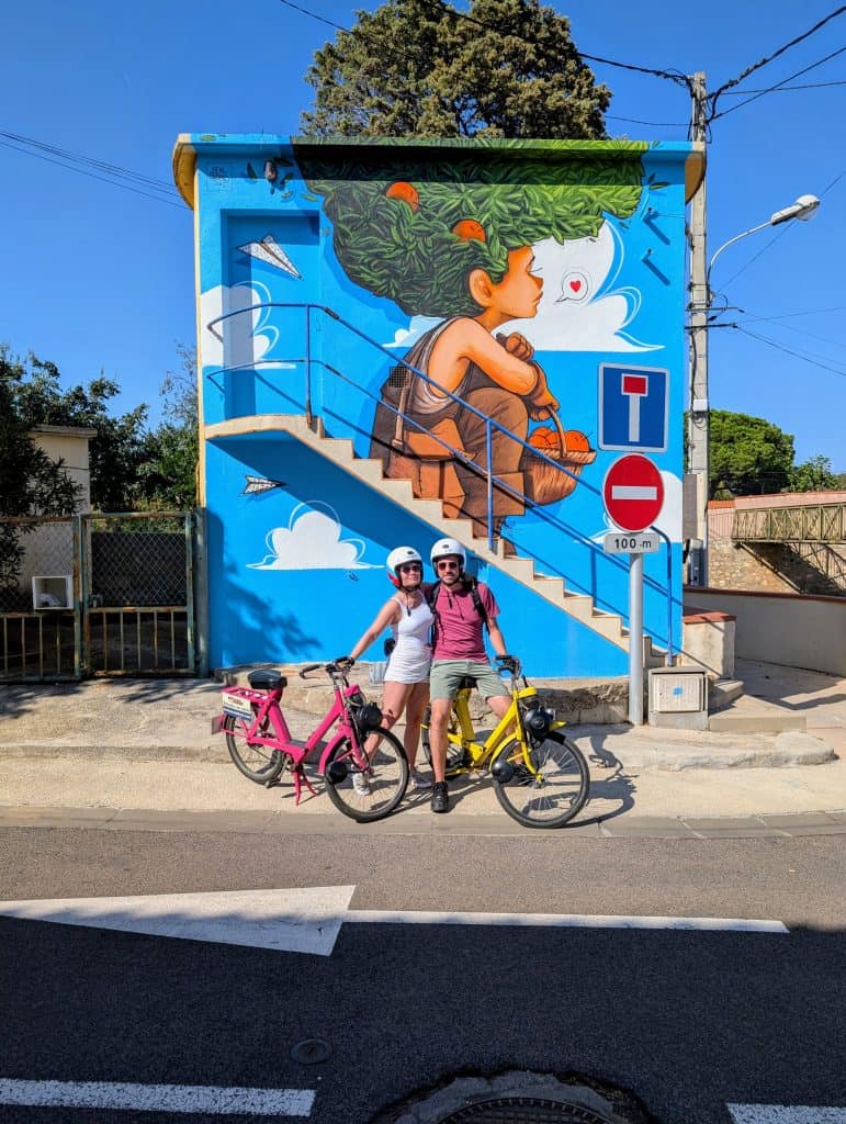 Couple en Solex posant devant une fresque du festival Urb’Art dans les rues d’Argelès-sur-Mer