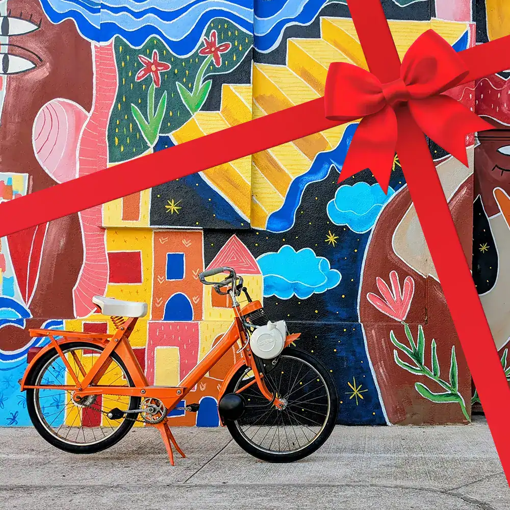 Solex garé devant une fresque très colorée de l’artiste Axelle Sodade dans une rue du village d’Argelès-sur-Mer