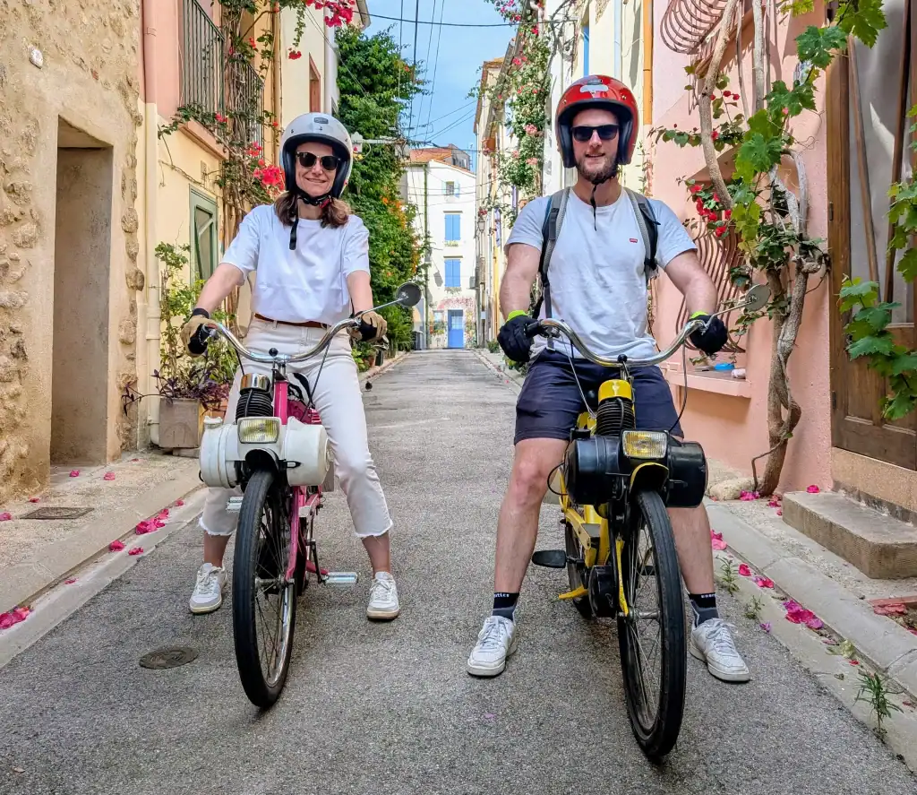 Couple circulant en Solex dans une rue fleurie et colorée du centre du village d’Argelès-sur-Mer