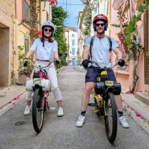 Couple circulant en Solex dans une rue fleurie et colorée du centre du village d’Argelès-sur-Mer
