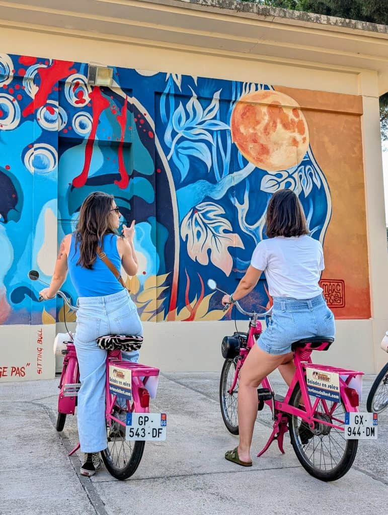 Deux amies en Solex devant une fresque du festival Urb’Art dans les rues d’Argelès-sur-Mer